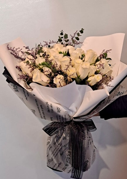 A hand-tied bouquet of 36 white roses accented with greenery and delicate fillers, wrapped in elegant black and white paper with a ribbon.