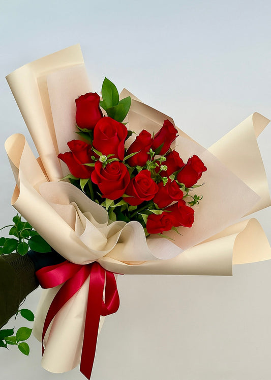 Elegant hand-tied bouquet of 12 red roses with lush greenery, symbolizing deep love and passion.