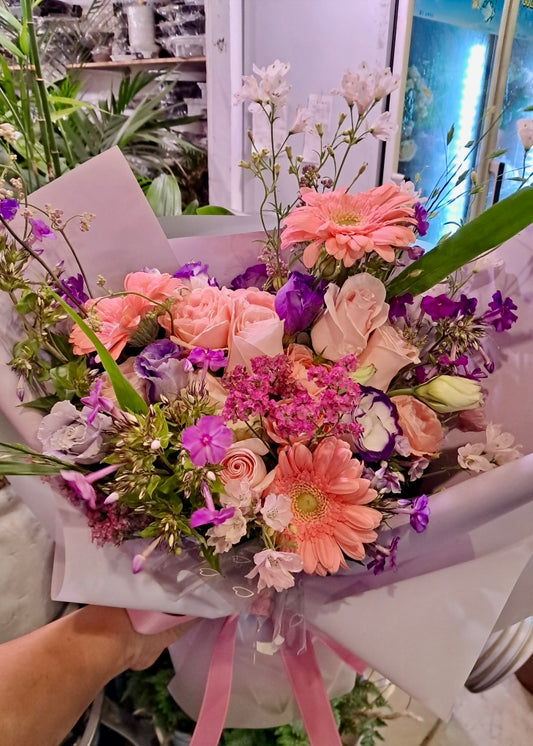 Pink and purple mixed flower bouquet beautifully wrapped in pastel paper.