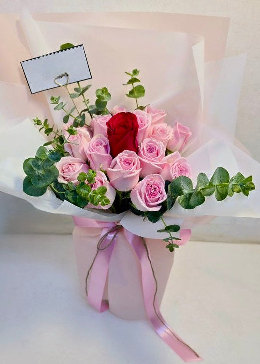 Romantic bouquet featuring seventeen soft pink roses surrounding a single red rose, accented with eucalyptus and wrapped in blush pink paper.