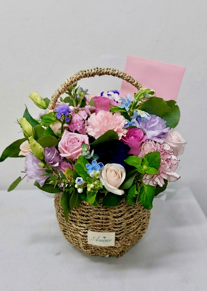 Pastel flower basket featuring pink roses and a mix of seasonal blooms with fresh greenery in a woven basket, perfect for birthdays, thank-you gifts, and everyday celebrations.