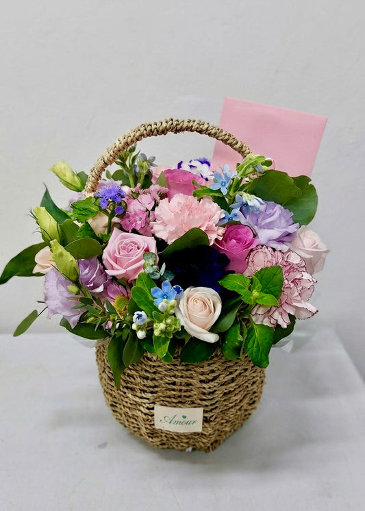 Pastel flower basket featuring pink roses and a mix of seasonal blooms with fresh greenery in a woven basket, perfect for birthdays, thank-you gifts, and everyday celebrations.