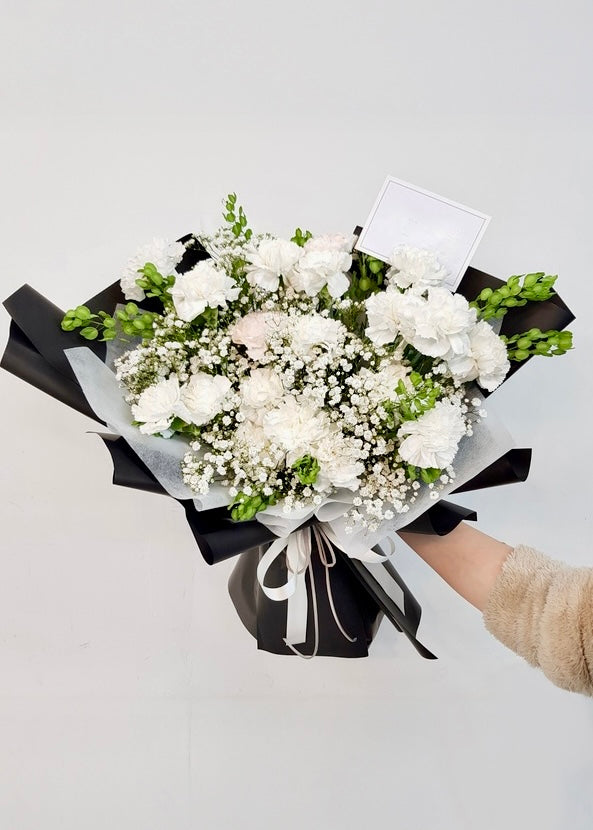 A serene white bouquet with carnations and delicate seasonal blooms, perfect for expressing purity, sympathy, or heartfelt wishes.