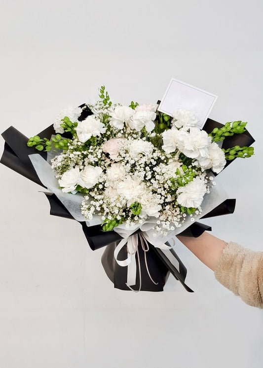 A serene white bouquet with carnations and delicate seasonal blooms, perfect for expressing purity, sympathy, or heartfelt wishes.