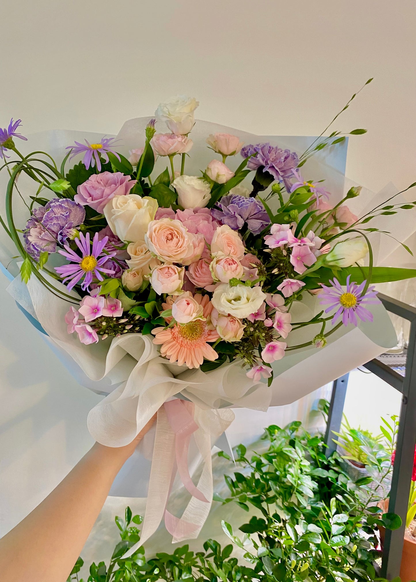 Hand-tied bouquet of soft pink and lavender flowers wrapped in pastel paper, ideal for sympathy, love, or everyday gifting.